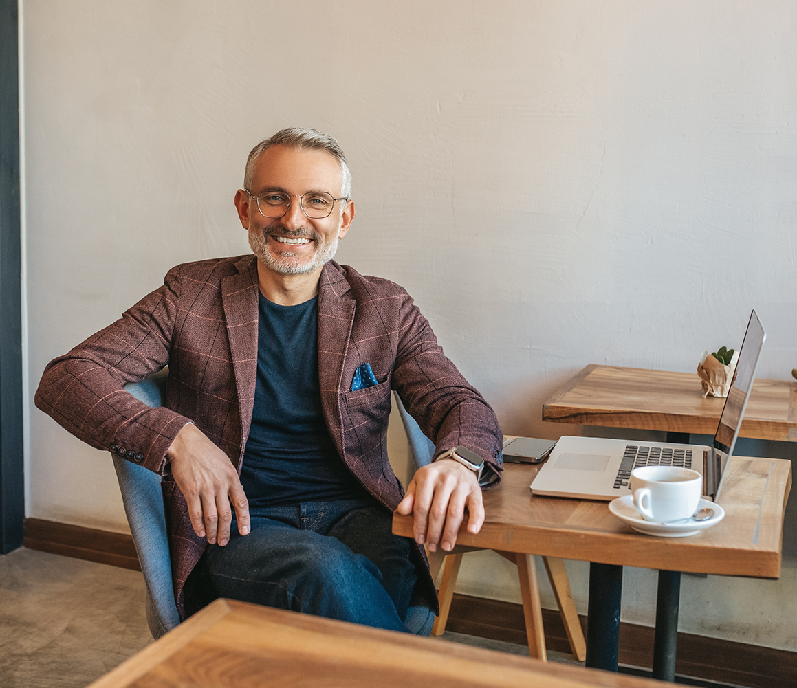 Man,Sitting,At,Table,Smiling,At,Camera